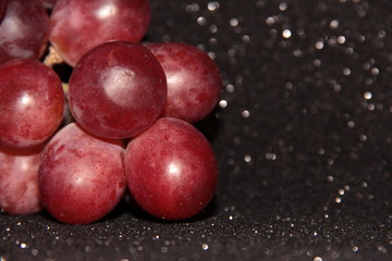 Large pink grapes on a black shiny background.