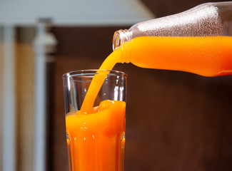 Pumpkin juice pours from a large bottle into a glass