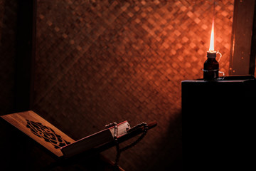 Quran and Islamic prayer beads in a rustic house room lit by traditional oil lamp. Concept of Ramadan in rural area.