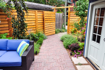 A private entrance to a small urban backyard garden shows beautiful plants, horizontal cedar...
