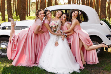 Happy wedding day. Beautiful bride and bridesmaids in pink dresses embracing with smile outdoors