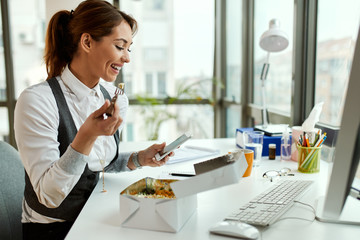 Happy businesswoman using mobile phone on lunch break in the office.
