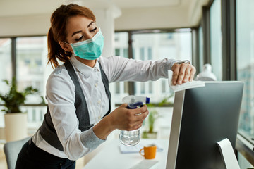 Businesswoman with face mask cleaning her computer in the office.