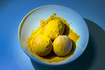 We paint chicken eggs in culinary spices of turmeric, a plate on a blue background
