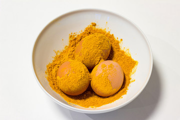 We paint chicken eggs in culinary spices of turmeric, a plate on a white background