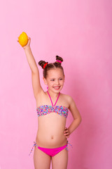 Caucasian beautiful little girl with fresh yellow lemons on a pink background.