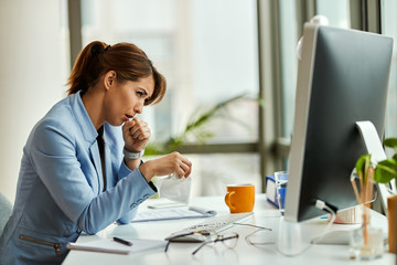 Young businesswoman coughing while working in the office.