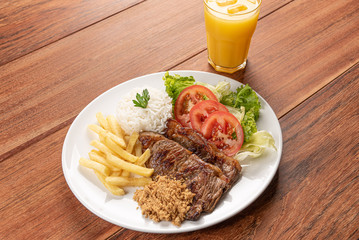 Beef steak with french fries, Beans and rice and a glass of orange juice on wooden table background, soft light