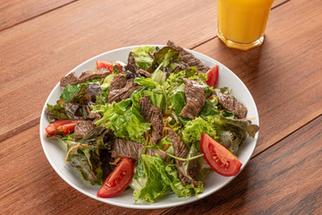 Fresh green salad with arugula,romaine, tomato, steak mignon and lettuce in a bowl on a wooden  background
