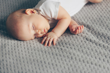 Sleeping baby boy in white bodysuit in bed with copyspace