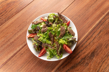 Fresh green salad with arugula,romaine, tomato, steak mignon and lettuce in a bowl on a wooden ...