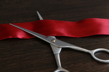 Red silk ribbon lies on metal scissors on the wooden wenge table. Theme of opening a new enterprise.