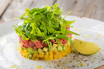 Delicious avocado, mango and raw salmon salad, tartare, served on a white plate with lime