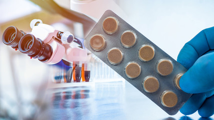 Packaging of tablets in close-up against the background of a microscope in a research laboratory.Pharmaceutical research.Laboratory for the development of medical products. Medicines quality assurance