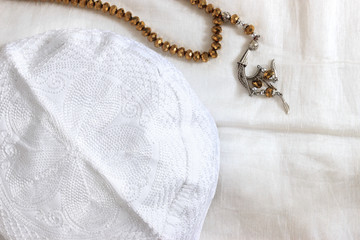 Fototapeta na wymiar Close up top wiew of golden prayer beads and white skullcap on white prayer rug. Muslim pray at home in Ramadan concept.