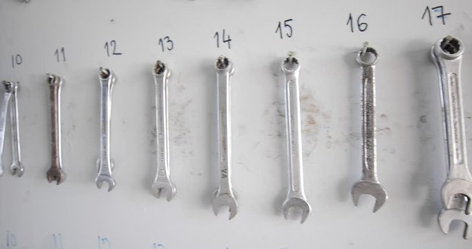 At a car mechanic-the shot is moving from left to right and shows his set of wrenches on a wall.