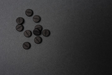 Close up of rough black round tablets in a light spot of dark grey surface