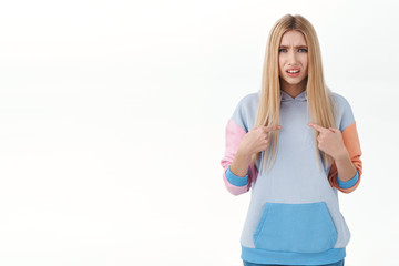 Frustrated and confused blonde glamour girl with blonde hair, looking offended or accused, pointing...