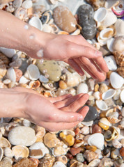 Male hands under a stream of water against the background of sea stones and shells.