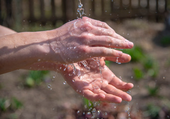 Strong male hands under a stream of water on a blurred natural background.