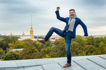 A happy young man is standing on the roof of a building on one leg. Joyful emotions and a smile....