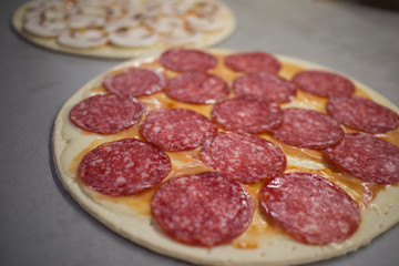 two round pizzas with different fillings with cheese, salami with mushrooms and tomatoes