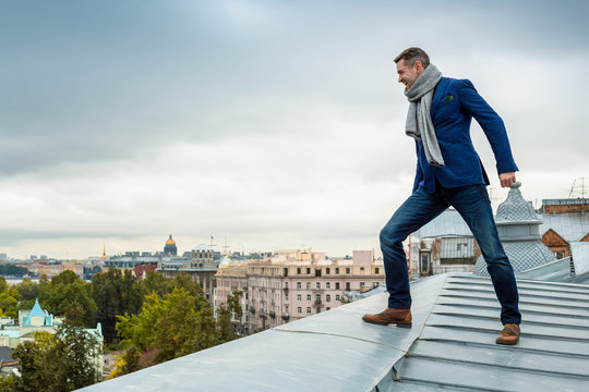 Happy stylish young man in jeans, a blue jacket and a scarf looks from the roof of the building at the sights of the historic center of a large European city. Saint-Petersburg, Russia.