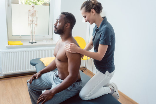 Physical therapist massaging a young black man on shoulder