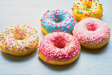 Assorted donuts with colorful frosted, pink glaze and sprinkles on blue table. Copy space
