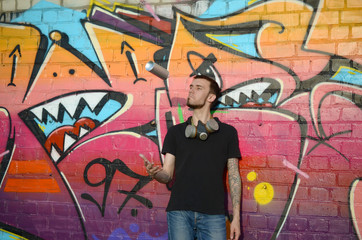 Young graffiti artist with gas mask on his neck throw his spray can against colorful pink graffiti on brick wall. Street art and contemporary painting process