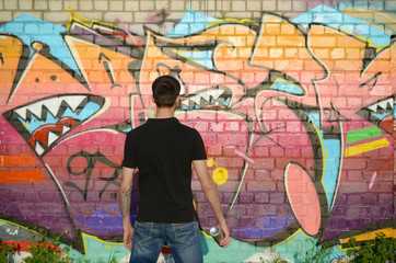 Young graffiti artist with backpack and gas mask on his neck paints colorful graffiti in pink tones on brick wall. Street art and contemporary painting process