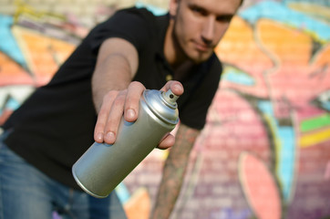 Young graffiti artist aims his spray can on background of colorful graffiti in pink tones on brick...