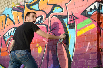 Young graffiti artist with backpack and gas mask on his neck paints colorful graffiti in pink tones...