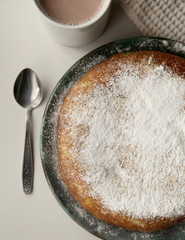Sweet round cake with powdered sugar. Cup of coffee.