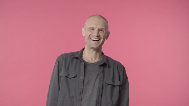 Handsome middle-aged bald man with bristle, looking curious with pleased grin at camera and start laughing at something hilarious, grey-haired elderly guy look after grandkids on playground
