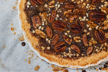 Top view of handmade pecan pie and nuts in a ceramic bowl, next to crispy dough crumbs.