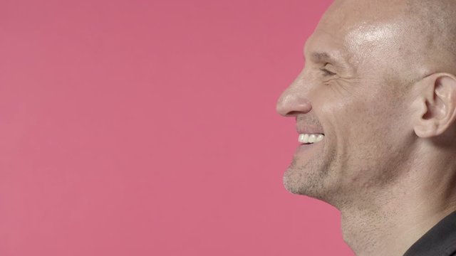 Profile headshot of middle-aged bald man with bristle, look left at blank pink copy space, start smile and laugh with approval, like something, delighted and rejoicing over good news
