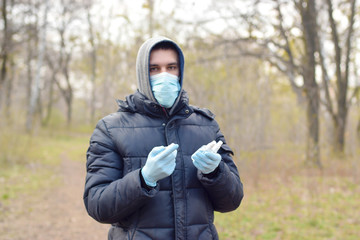 Young man in protective mask shows sanitizer spray bottles outdoors in spring wood