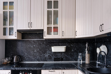 White wall cabinets in the kitchen with a black countertop. Placed dishes and kitchen utensils on...