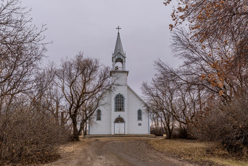 Fototapeta na wymiar The vintage St. Charles Roman Catholic Church surrounded by trees in Coderre, Saskatchewan, Canada