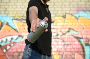 Young graffiti artist aims his spray can on background of colorful graffiti in pink tones on brick...