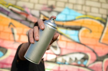 Young graffiti artist aims his spray can on background of colorful graffiti in pink tones on brick...