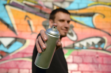 Young graffiti artist aims his spray can on background of colorful graffiti in pink tones on brick...
