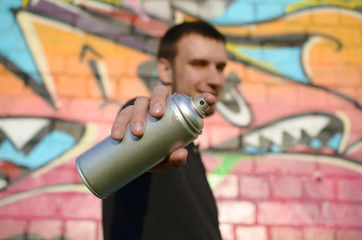 Young graffiti artist aims his spray can on background of colorful graffiti in pink tones on brick...