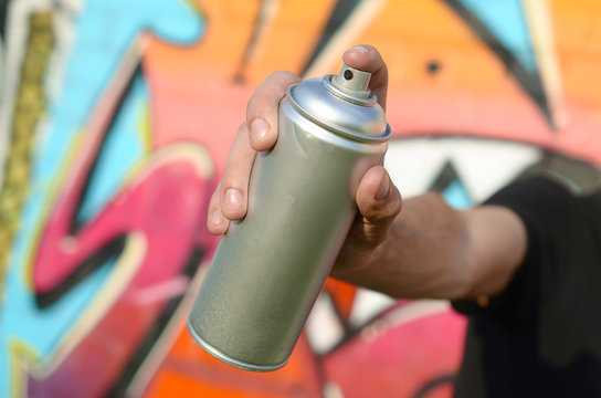 Young graffiti artist aims his spray can on background of colorful graffiti in pink tones on brick wall. Street art and contemporary painting process