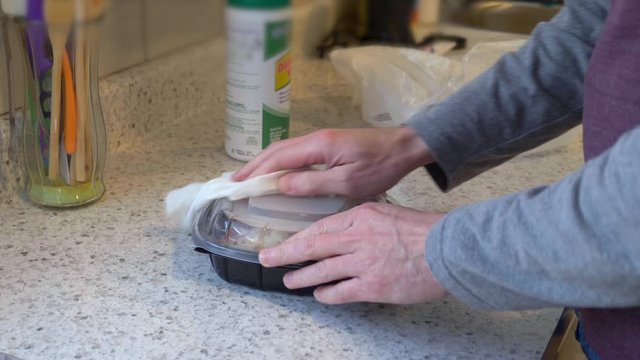 A man removes his takeout food container out of a bag and cleans it with sanitizing wipes. Cleaning surfaces was a common practice to stop the spread of COVID-19 during the pandemic of 2020.  	