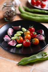 cherry tomato, broad beans and garlic in black dish - closeup