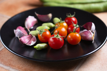 cherry tomato, broad beans and garlic in black dish - closeup