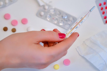 A woman's hand holds a thermometer over a table with pills, concept