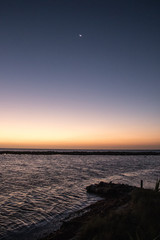 Sunrise over beach in Hawaii with crescent moon in purple sky over golden glow at the horizon